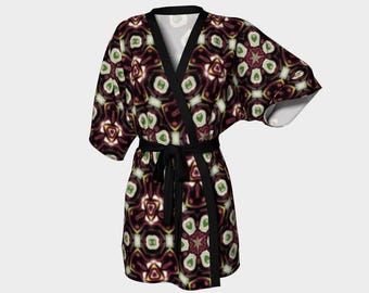 Puede incluir: Una bata de kimono con estampado negro y rojo con una faja negra. La bata tiene un patrón geométrico con detalles en verde, blanco y amarillo.