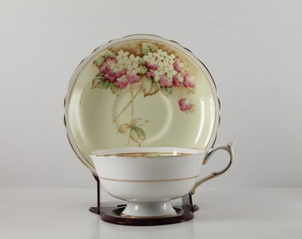 May include: A white teacup and saucer with a floral design. The saucer has a pale yellow background with a pink and white floral pattern. The teacup has a white background with a gold trim.