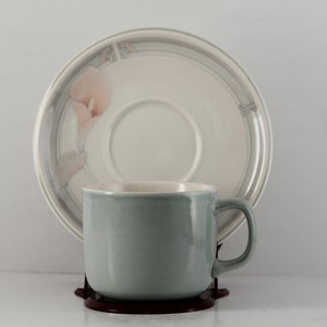 May include: A light blue ceramic teacup with a floral design on the saucer. The saucer is white with a gray border and a floral design.