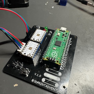 Peut inclure: Une carte de circuit imprimé noire avec un micro-ordinateur Raspberry Pi vert, deux pilotes de moteur pas à pas et un bouton rouge. La carte porte l'inscription "V.1.0 @3DPRINTADVENTURES".