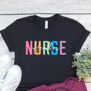 May include: A black t-shirt with the word "NURSE" in rainbow colors and the word "Heather" written underneath. The shirt is laying on a white wooden surface with a pair of white sneakers, a stethoscope, and a potted plant.