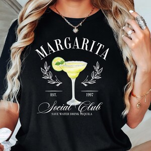 May include: Black t-shirt with white text that reads "Margarita Social Club Est. 1997 Save Water Drink Tequila". The shirt features a graphic of a margarita glass with a lime wedge.