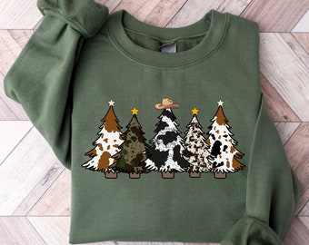 May include: Green sweatshirt with a design of five Christmas trees. The trees are decorated with cowhide, camouflage, and a cowboy hat.