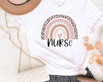May include: White t-shirt with a rainbow graphic and the word "nurse" printed on it. The rainbow is made of pink, brown, and leopard print. The shirt is paired with a black skirt with white polka dots and brown ankle boots.