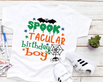 May include: White t-shirt with a green and orange graphic that says "Spooktacular birthday boy" with a spider and web design.