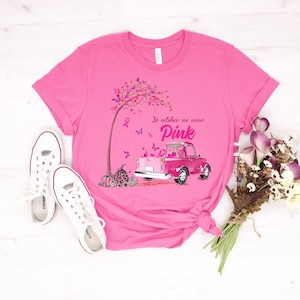 May include: Pink t-shirt with a pink truck carrying pink ribbons and pumpkins. The truck is driving through a pink tree with butterflies. The text on the shirt reads "In October we wear Pink".