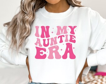 May include: White cropped sweatshirt with pink lettering that reads "In My Auntie Era".
