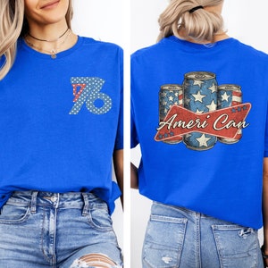 May include: A royal blue t-shirt with a white and red design of three cans of beer with stars and stripes. The text "Ameri Can" is printed on the shirt. The front of the shirt has a white and blue design of the number 76.