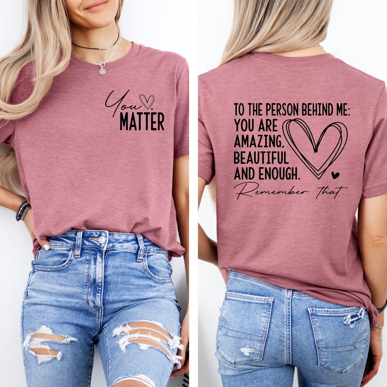 May include: A mauve t-shirt with the text "You Matter" on the front and the text "To the person behind me: You are amazing, beautiful and enough. Remember that." on the back. The shirt is being modeled by a person wearing blue jeans.