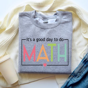 May include: Gray sweatshirt with the text "it's a good day to do MATH" in a colorful rainbow font. The letters are outlined in black and there is a small pink heart below the word MATH.