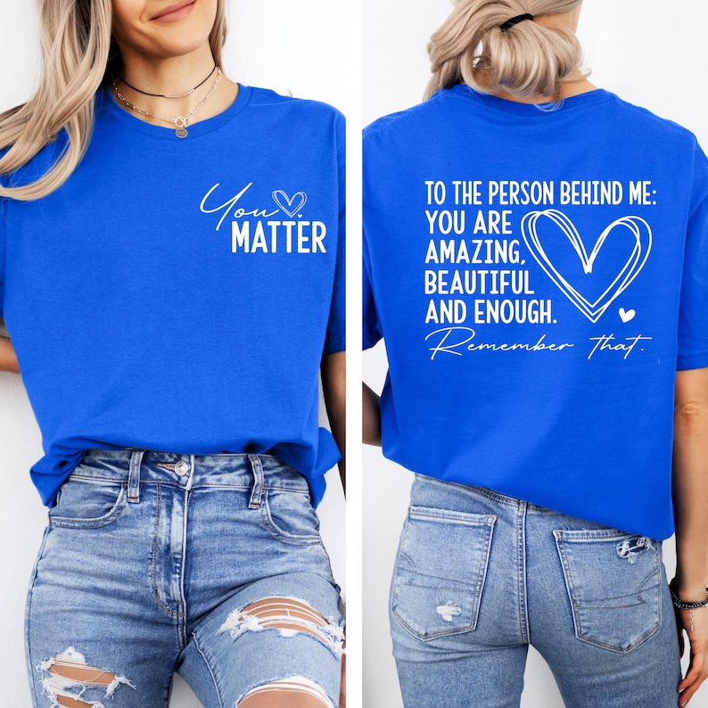 May include: A royal blue t-shirt with white text that reads "You Matter" on the front and "To the person behind me: You are amazing, beautiful and enough. Remember that." on the back. The shirt is being modeled by a person wearing blue jeans.