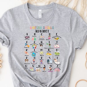 May include: A gray t-shirt with a colorful alphabet chart featuring coping skills for children. Each letter of the alphabet is paired with a coping skill, such as breathing, dancing, and taking a nap. The chart is surrounded by a white border.