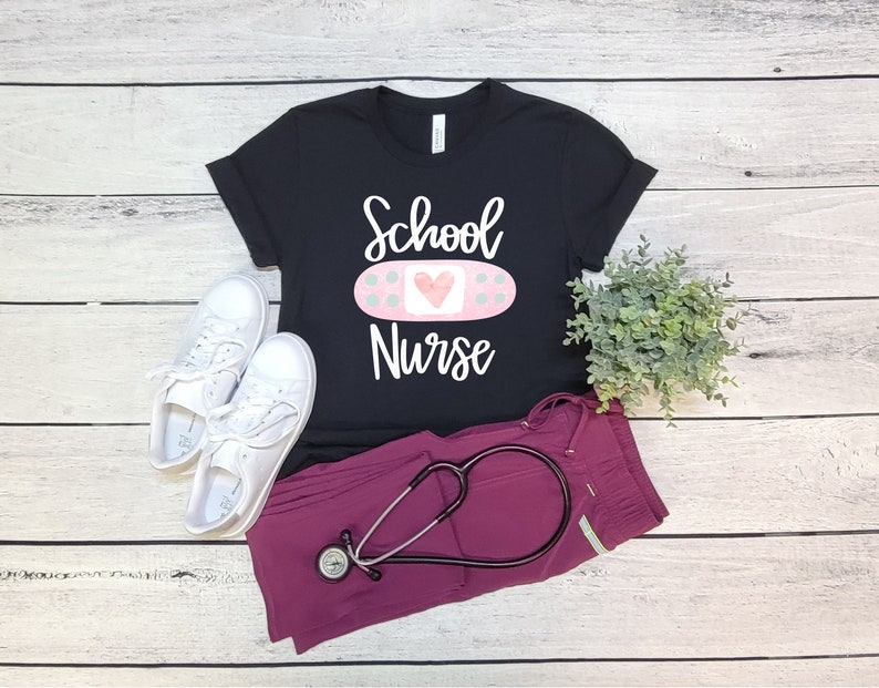 May include: Black t-shirt with the text "School Nurse" and a pink bandage with a heart on it. A stethoscope and scrubs are also pictured.