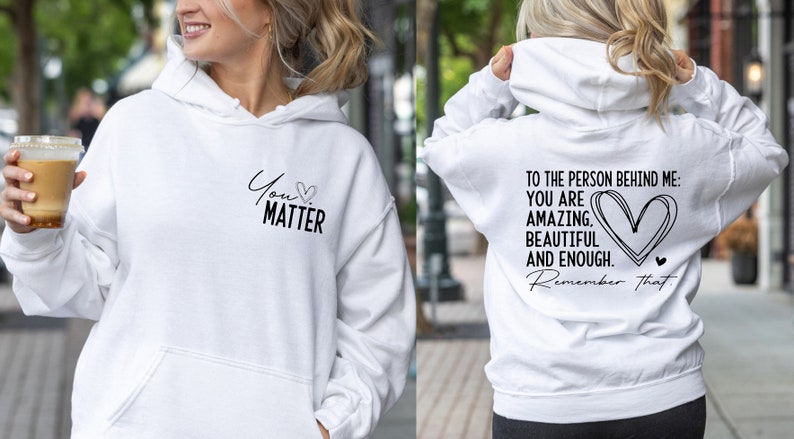 May include: White hoodie with a black graphic on the front that says "You Matter" with a heart symbol. The back of the hoodie has a black graphic that says "To the person behind me: You are amazing, beautiful and enough. Remember that." with a heart symbol.