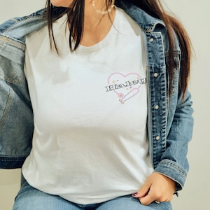 K&ouml;nnte beinhalten: Ein wei&szlig;es T-Shirt mit einem rosafarbenen Herzdesign, auf dem der Name "Haley" in schwarzer Schrift steht. Das Herz hat einen rosafarbenen Umriss und ein kleines, stilisiertes Skateboard im Inneren. Das T-Shirt wird von einer Person getragen, die eine blaue Jeansjacke tr&auml;gt.