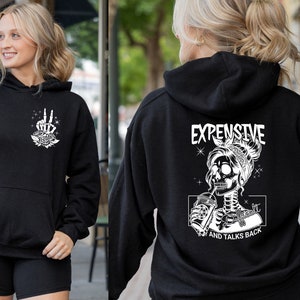 May include: Black hoodie with a white graphic of a skeleton woman drinking from a cup with the text "Expensive and Talks Back".
