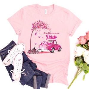 May include: Pink t-shirt with a pink truck carrying pumpkins and a pink ribbon tree. The text on the shirt reads "In October we wear Pink".