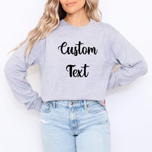 A woman wearing a grey sweatshirt with the text "Custom Text" printed on it, standing against a white background.