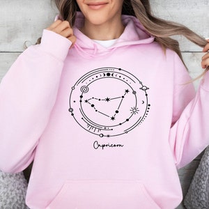 May include: Pink hoodie with a black graphic of the Capricorn constellation and the word "Capricorn" written below.