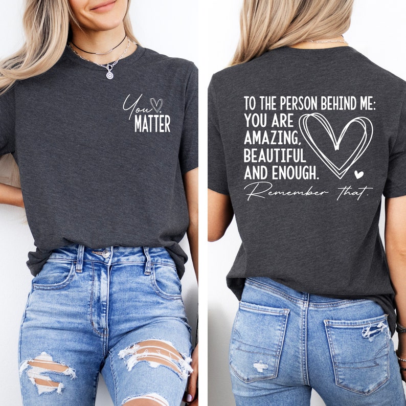 May include: A dark gray t-shirt with a white graphic on the front that says "You Matter" with a heart symbol. The back of the shirt has a white graphic that says "To the person behind me: You are amazing, beautiful and enough. Remember that." with a heart symbol.