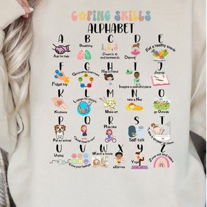 May include: A beige sweatshirt with a colorful graphic of the alphabet. Each letter is paired with a coping skill, such as breathing, dancing, and taking a nap. The text "Coping Skills Alphabet" is at the top of the graphic.