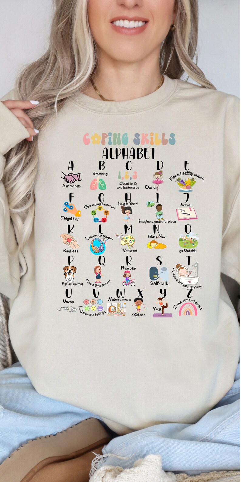 May include: A beige sweatshirt with a colorful graphic of the alphabet. Each letter is paired with a coping skill, such as breathing, dancing, and taking a nap. The text "Coping Skills Alphabet" is at the top of the graphic.