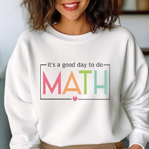 May include: White sweatshirt with the text "it's a good day to do MATH" in a colorful rainbow font with a small pink heart below the text.