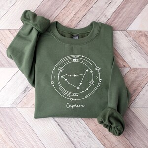 May include: A green sweatshirt with a white graphic of the Capricorn constellation and the word "Capricorn" printed below it.
