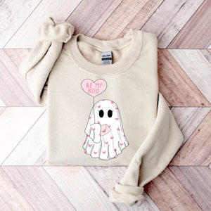 May include: A beige sweatshirt with a graphic of a ghost holding a heart-shaped balloon that says "Be My Boo".