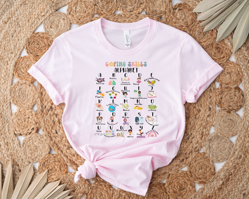 May include: Pink t-shirt with a graphic of a colorful alphabet with coping skills for each letter. The graphic says "Coping Skills Alphabet".