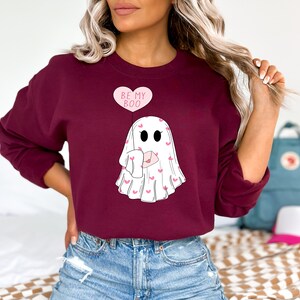May include: A maroon sweatshirt with a white ghost holding a pink envelope with hearts. The ghost has a pink balloon that says "Be My Boo".