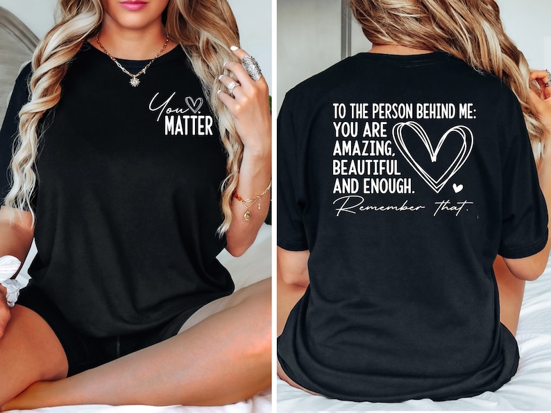 May include: Black t-shirt with a white graphic on the front that says "You Matter" with a heart symbol. The back of the shirt has a white graphic that says "To the person behind me: You are amazing, beautiful and enough. Remember that." with a heart symbol.