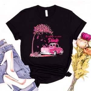 May include: Black t-shirt with a pink truck and a pink tree with pink ribbons. The text on the shirt reads "In October we wear Pink".