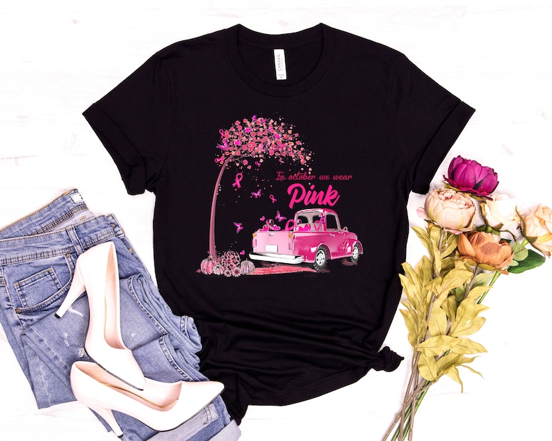May include: Black t-shirt with a pink truck and a pink tree with pink ribbons. The text on the shirt reads "In October we wear Pink".