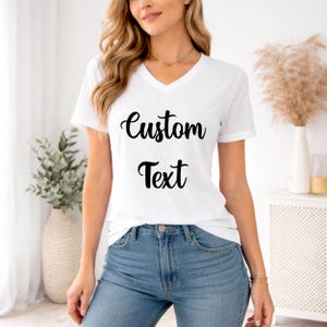 A woman wearing a white t-shirt with the text "Custom Text" printed on it, standing in a room with a potted plant and a vase.