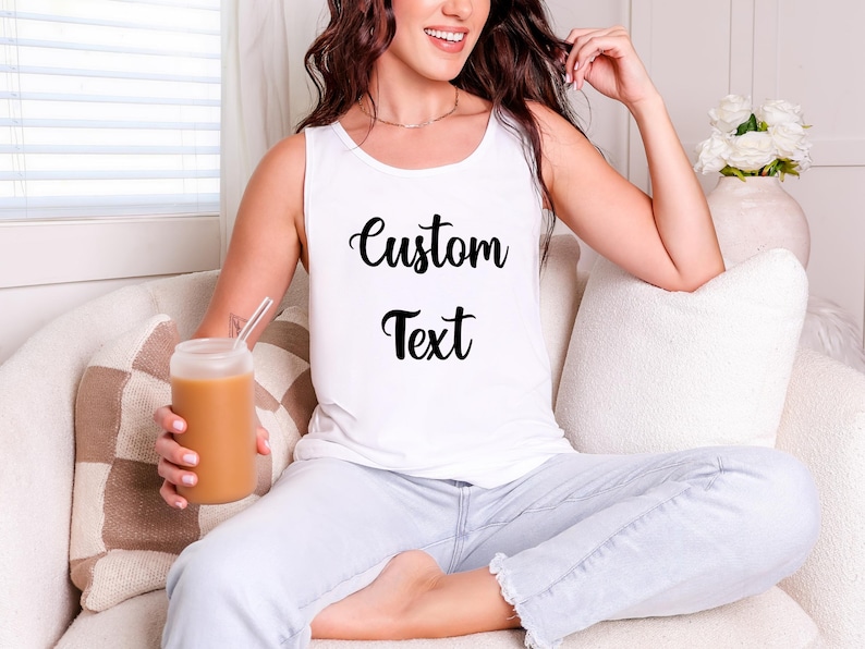 A woman sitting on a couch, wearing a white tank top with the text "Custom Text" printed on it, and holding a drink in a glass.