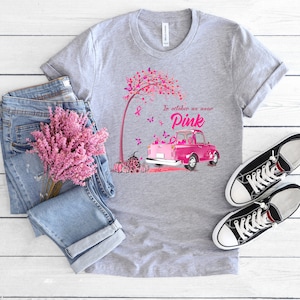 May include: A gray t-shirt with a pink truck and a pink tree with butterflies. The text on the shirt reads "In October we wear Pink".