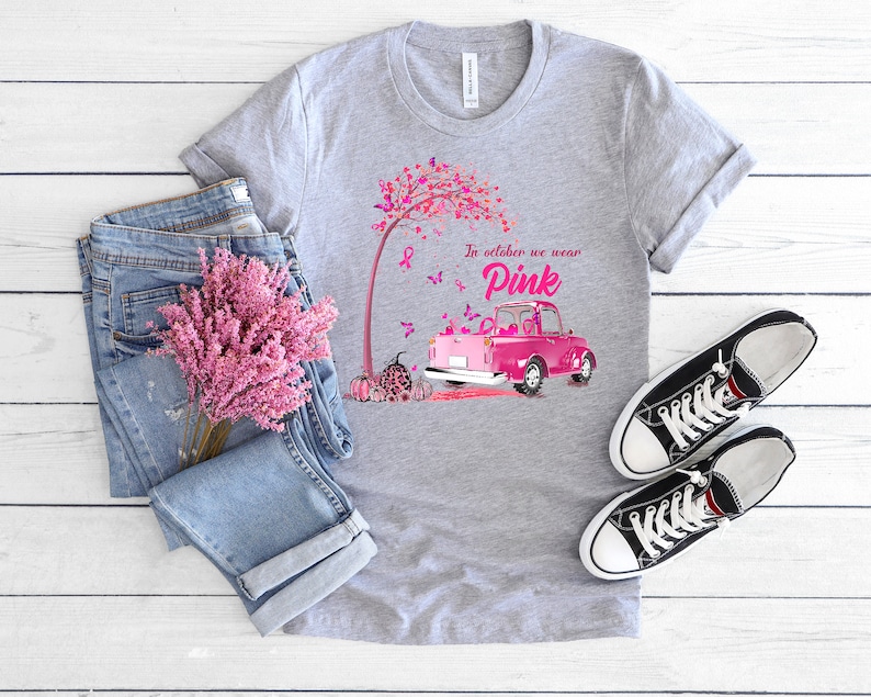 May include: A gray t-shirt with a pink truck and a pink tree with butterflies. The text on the shirt reads "In October we wear Pink".