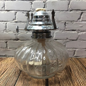 May include: A clear glass oil lamp with a ribbed design and a silver metal wick holder.