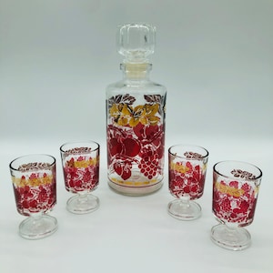 Puede incluir: Un juego de cuatro vasos de chupito de vidrio transparente con diseños de frutas rojas y doradas y una jarra a juego.