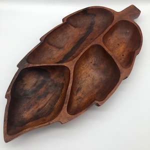 May include: A wooden serving tray shaped like a leaf with five separate compartments. The tray is dark brown and has a natural wood finish.