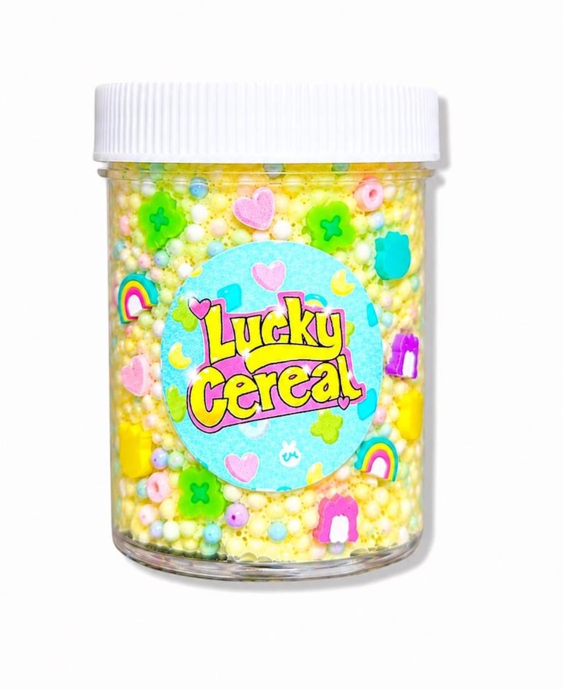 May include: A clear plastic jar filled with yellow sprinkles and colorful candy shapes, including hearts, rainbows, and clovers. The jar has a white lid and a label that reads "Lucky Cereal" in a playful font.