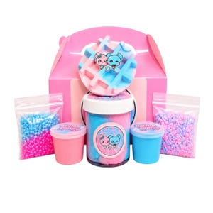May include: A pink gift box with a waffle-shaped topper in pink and blue. The set includes a large jar and two small containers of blue and pink slime, plus two bags of colorful beads. The jars have a cartoon bear logo.