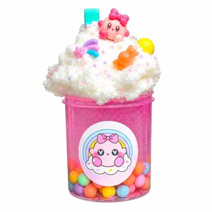 Könnte beinhalten: Ein durchsichtiger rosa Behälter gefüllt mit farbigem Schleim und kleinen Süßigkeiten. Der Behälter ist mit weißem, flauschigem Schleim bedeckt und mit kleinen Spielzeugen verziert. Auf der Vorderseite befindet sich ein Aufkleber mit einer Cartoonfigur.