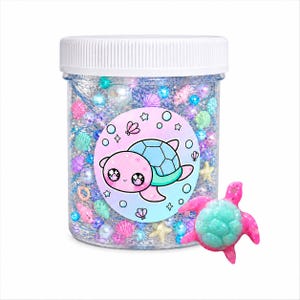 May include: A clear plastic jar filled with glitter, beads, and small sea-themed decorations. A round sticker with a cartoon turtle is on the jar. A small pink and teal turtle figurine is next to the jar.