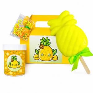 May include: A yellow gift box with a pineapple theme. Includes a jar of yellow slime with pineapple chunks, a pineapple-shaped lollipop with a green bow, and a bag of colorful sprinkles. The box has a pineapple sticker.