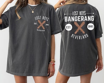 May include: A dark gray t-shirt with a graphic print of a crossed pair of wooden sticks with the text "Lost Boys Bangerang" and "Est. 1991 Neverland".
