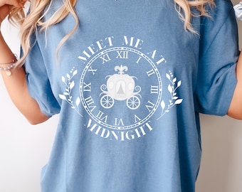 May include: A light blue t-shirt with a white graphic design featuring a clock face with a carriage inside and the text "MEET ME AT MIDNIGHT".