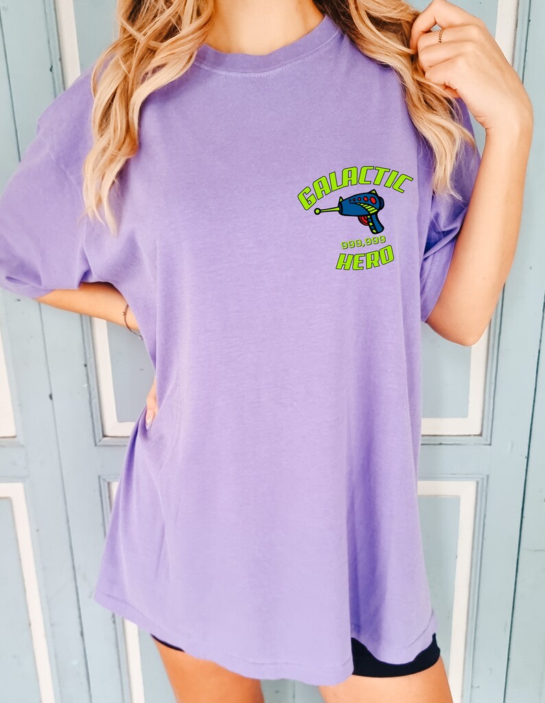 May include: A purple t-shirt with a graphic of a blue space gun and the text "GALACTIC HERO" in green.