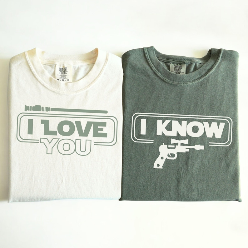 May include: Two t-shirts with a Star Wars theme. The white t-shirt has a lightsaber and the text "I LOVE YOU". The green t-shirt has a blaster and the text "I KNOW".
